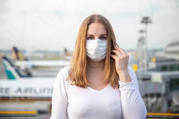 Retrato de una hermosa chica caucásica en una máscara médica respiratoria mirando a la cámara. en los aviones de fondo y el aeropuerto en desenfoque. concepto epidémico de coronavirus, covid-19 . — Foto de Stock