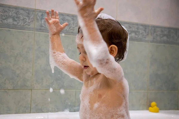 목욕하는 귀여운 여자 애. 재미있는 아기가 욕조에서 비누 거품을 가지고 노는 거야. 가까이 다가가서, 부드럽게 초점을 맞추고, 뒤로는 푸른 욕실 이 있습니다.. — 스톡 사진