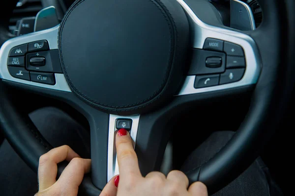 De vinger van een vrouwelijke hand wijst naar de knop van het verwarmde stuurwiel op het multifunctionele stuurwiel, de uitrusting van een moderne auto. close-up, zachte focus, wazige achtergrond. — Stockfoto