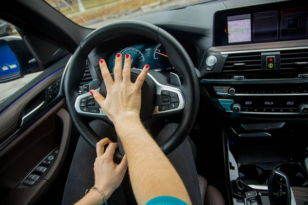 nervous situation on the road concept. woman with her right hand presses horn on the steering wheel and drives a modern car with a black interior. girl rides in her car.close-up, blur background