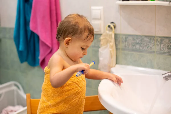 Маленька мила дитина, 13 років, стоїть на стільці у ванній кімнаті, загорнутій помаранчевим рушником з зубною щіткою і вчиться чистити зуби. крупним планом, м'який фокус, розмитий фон — стокове фото