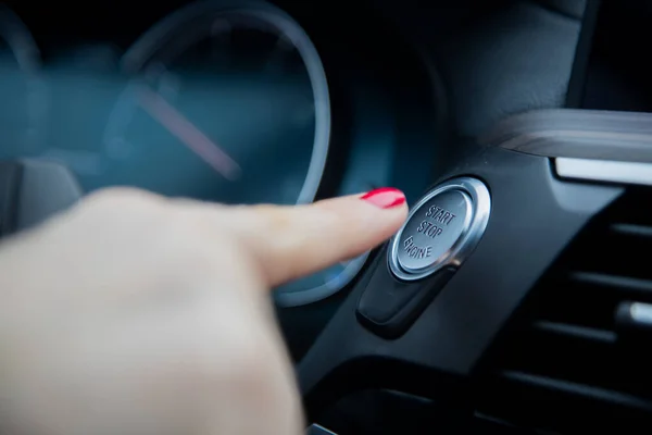Kadın parmakları bir arabanın torpido gözünde motoru durdurma düğmesine basıyor. yakın plan, yumuşak odak, arka planda gösterge paneli ve araç hız göstergesi bulanık, yan görünüm