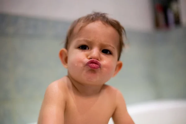 Banyo yapan şirin bir bebek öpücük gösterir ve kameraya bakar. Yumuşak odaklı, yakın plan, arka plan - evdeki bulanık banyo — Stok fotoğraf