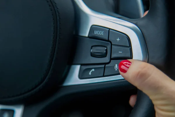 Finger einer weiblichen Hand drücken den Mikrofonknopf am Lenkrad, die Ausstattung eines modernen Autos. Nahaufnahme, weicher Fokus, unscharfer Hintergrund — Stockfoto