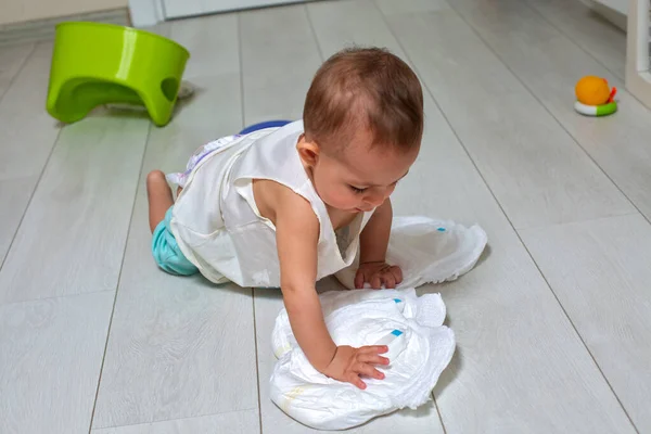 potty training concept. A cute little baby in a room on the bright floor plays with a diaper and an inverted green pot. soft focus