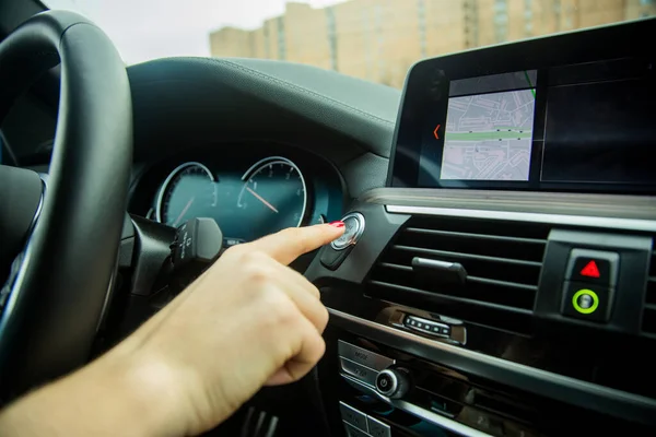 female finger presses start stop engine button on a car dashboard. close-up, soft focus, in the background car interior details in blur, side view