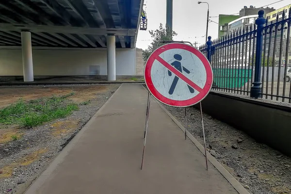 Das Schild, auf dem die Durchfahrt verboten ist, steht auf einem gepflasterten Fußweg. Im Hintergrund die linke untere Brücke, rechts ein schwarzer Zaun und die Stadt in Unschärfe. — Stockfoto