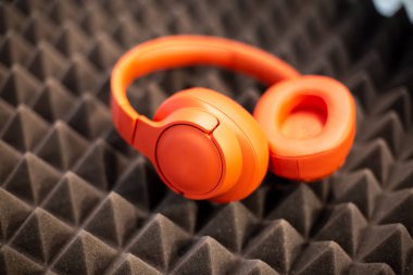 Turuncu kablosuz kablosuz monitör kulaklıkları koyu köpüklü lastik ses geçirmez panelde duruyor. Yumuşak odaklanma, bulanık arkaplan.
