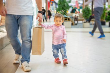 Kara Cuma konsepti, çocuklarla alışveriş. Babasıyla birlikte küçük şirin bir kız alışveriş için bir kağıt torba tutuyor ve kameraya bakıyor. Yakın plan, yumuşak odak, arka planda bulanık bir alışveriş merkezi.