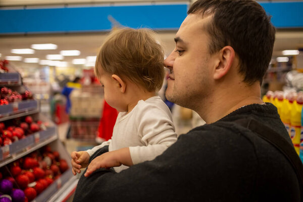 A man with love smile holds a small cute baby in his arms in a store of christmas new year decoration balls for christmas tree. close-up, soft focus, blur background