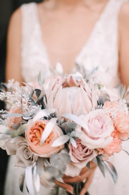 Beyaz, pembe, mor, lavanta tonları olan gül, karanfil, protein ve gümüş yapraklardan oluşan gelin buketine yakın çekim. Gelin elinde dantelli beyaz bir elbiseyle bir buket tutuyor..