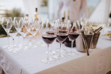 Masada şampanya ile birlikte birçok bardak var. Masa beyaz bir masa örtüsüyle kaplıdır.