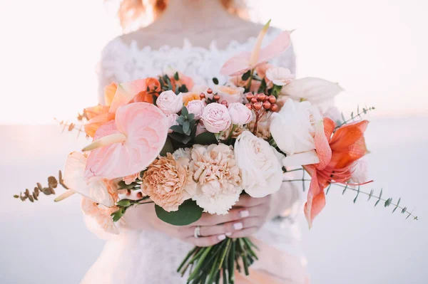 白い桃の色合いでアマリリス アンスリウム カーネーション ユーカリの花嫁の花束のクローズアップ レースの白いドレスの花嫁は彼女の手に花束を持っています 白い砂 — ストック写真