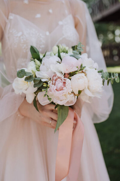 Bride's bouquet close-up, the bouquet consists of white and pink peonies, eucalyptus. The bride dressed in pink wedding dress holds the bouquet 