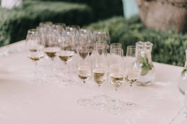 Masada şampanya ile birlikte birçok bardak var. Masa beyaz bir masa örtüsüyle kaplıdır.