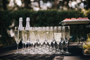 Masada şampanya ile birlikte birçok bardak var. Masa beyaz bir masa örtüsüyle kaplıdır.
