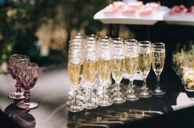 Masada şampanya ile birlikte birçok bardak var. Masa beyaz bir masa örtüsüyle kaplıdır.