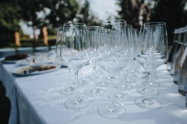 Masada birçok boş kırmızı şarap kadehi var. Masa beyaz bir masa örtüsüyle kaplıdır.