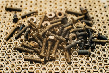 Yakın plan, makro. Eski Sovyet pirinçleri, düz başlı tornavidayla kafa vidalarını batırdı. Pirinç cevizlerinin dokusu, arkaplanı bal peteği şeklinde dizilmiş. Altın renkli vidalar. Kirli odun vidaları