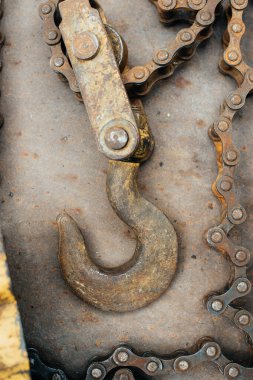 Paslı Sovyet ev yapımı vinç, sarı boya izleri var. Kanca, bisiklet zinciri, zincir halkalar. Vinç paslı demir bir yaprağın üzerinde yatıyor. Hurda metal. Yakın plan. Makro