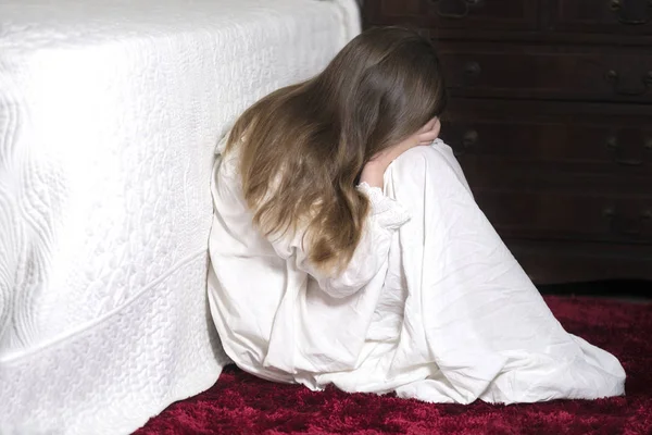 image covering the  Social Issues of child abuse,  Young unrecognisable girl is a affluent bedroom setting holding her head in her hands  copy space for text
