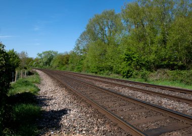 Paralel tren yolu manzarası. Etrafı yemyeşil ağaçlar ve çalılarla çevrili. Mavi gökyüzündeki boşluğu kopyalayın. 
