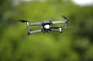 Kameralı modern insansız hava aracı yeşil yaz kırsalının bulanık arka planında uçarak doğayı keşfediyor.