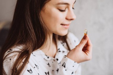 Diyet olsun. Beslenmek. Gülümseyen kız Omega-3 morina ciğeri ile hap alıyor ve sabahları elinde bir bardak taze su tutuyor. Sağlıklı beslenme ve yaşam tarzı kavramı. D vitamini, E vitamini, Balık yağı kapsülleri.