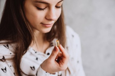 Diyet olsun. Beslenmek. Omega-3 morina ciğeri ile hap alan ve sabahları elinde bir bardak taze su tutan bir kız. Sağlıklı beslenme ve yaşam tarzı kavramı. D vitamini, E vitamini, Balık yağı kapsülleri.