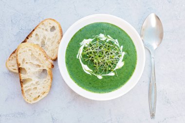 Kremalı taze ıspanak çorbası ve açık gri zemin üzerinde ciabatta ekmeği olan beyaz bir tabakta roka yeşili. Sağlıklı ve diyet yiyecekler. Düz yatıyordu.