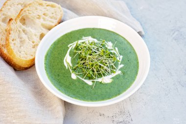 Kremalı taze ıspanak çorbası ve açık gri zemin üzerinde ciabatta ekmeği olan beyaz bir tabakta roka yeşili. Sağlıklı ve diyet yemekleri.