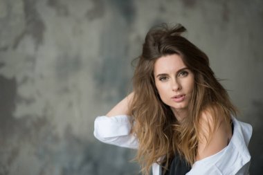 Uçan saçları ve gri arka planda beyaz gömleği olan dolgun dudakları olan zarif bir kız kameraya dikkatsizce bakıyor. Güzellik ve modaya uygun bir tarz. Yumuşak seçici odak.