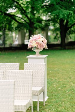 Taş bir vazodaki güzel bir buket çiçek yeşil bir arka plandaki bir sütunun üzerinde duruyor. Düğün töreni için dekor. Dikey