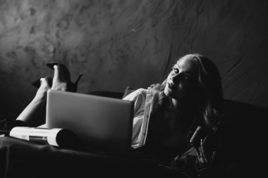 Elinde kamera ve yatağında dizüstü bilgisayarla güzel bir kadın fotoğrafçı. Gösterişsiz siyah beyaz resim. Yumuşak seçici odaklanma. Evden çalış..