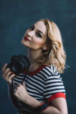 Fotoğraf stüdyosunda elinde kamerayla genç ve güzel bir fotoğrafçı kız. Kadın işi bir hobidir. Yumuşak seçici odak.