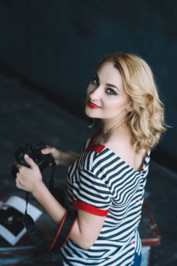 Fotoğraf stüdyosunda elinde kamerayla genç ve güzel bir fotoğrafçı kız. Kadın işi bir hobidir. Yumuşak seçici odak.