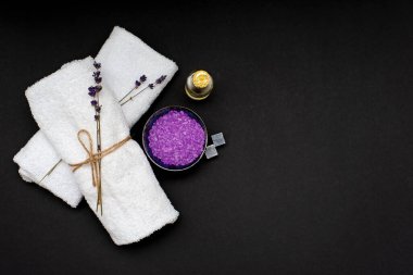 Spa konsepti. Rahatlatıcı bir banyo için lavanta tuzu, aroma yağı, beyaz havlular ve siyah arka planda kuru lavanta çiçekleri. Aromaterapi yatıyordu..