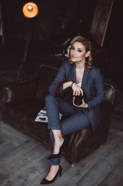 Siyah arka planda takım elbiseli, kendine güvenen güzel bir iş kadınının portresi elinde bir kamera tutuyor. Cinsiyet eşitliği kavramı. Güçlü, bağımsız bir kadın. Yumuşak seçici odak.