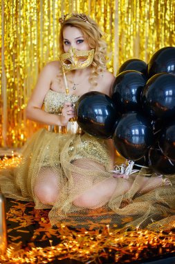 Güzel genç kız model sarışın elinde nilüfer çiçeğinin arka planında kornalar olan zarif altın bir elbise giymiş bir karnaval maskesi tutuyor. .