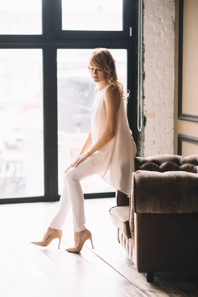 白いズボン ブラウス 窓の近くのロフトスタジオでの靴で巻き毛の美しい若い細いブロンドの女性 柔らかい選択的フォーカス — ストック写真