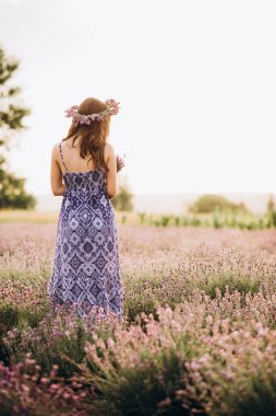 Uzun elbiseli güzel bir kız ve gün batımında lavanta tarlasında bir çelenk..