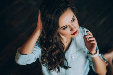 Mükemmel siyah kıvırcık saçlı, güzel makyajlı, kot gömlekli, kırmızı dudaklı güzel bir genç kadın. Yumuşak seçici odak.