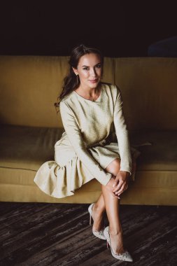 Koyu kıvırcık saçlı, kahverengi gözlü, altın rengi elbisesi olan güzel, genç, esmer bir kadın çatı katındaki hardal kanepesinde oturuyor. Yumuşak seçici odak.