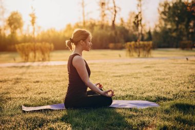 36 yaşında beyaz bir kadın sabahın erken saatlerinde çimenlerde çiğ taneleriyle yoga yapıyor. Sağlıklı yaşam tarzı kavramı. Sabah meditasyonu, rahatlama. Yumuşak seçici odak.