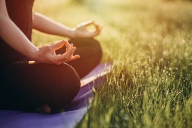 Genç beyaz kadın, çimen ve çiy dolu bir ormanda güneşli bir sabahta nilüfer pozisyonunda yoga yapıyor. Sağlıklı yaşam tarzı kavramı. Sabah meditasyonu, rahatlama. Yumuşak seçici odak.