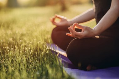 Genç beyaz kadın, çimen ve çiy dolu bir ormanda güneşli bir sabahta nilüfer pozisyonunda yoga yapıyor. Sağlıklı yaşam tarzı kavramı. Sabah meditasyonu, rahatlama. Yumuşak seçici odak.