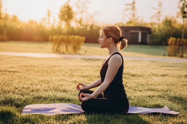 A 36-year-old young Caucasian woman practices yoga on an early sunny morning on grass with dew. Healthy lifestyle concept. Morning meditation, relaxation. Soft selective focus.