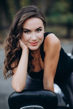 Siyah kolsuz tişörtlü ve deri pantolonlu güzel motorcu kız motosikletin arkasında oturuyor. Hız ve özgürlük kavramı. Yumuşak seçici odak.