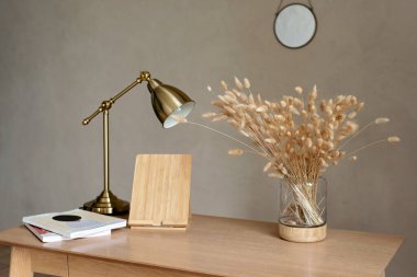 Doğal ahşap masa, bej renkli modern tarzda, vazo dolusu kurutulmuş çiçek ve bakır lamba ile. İçişleri Bakanlığı. İç Tasarım.