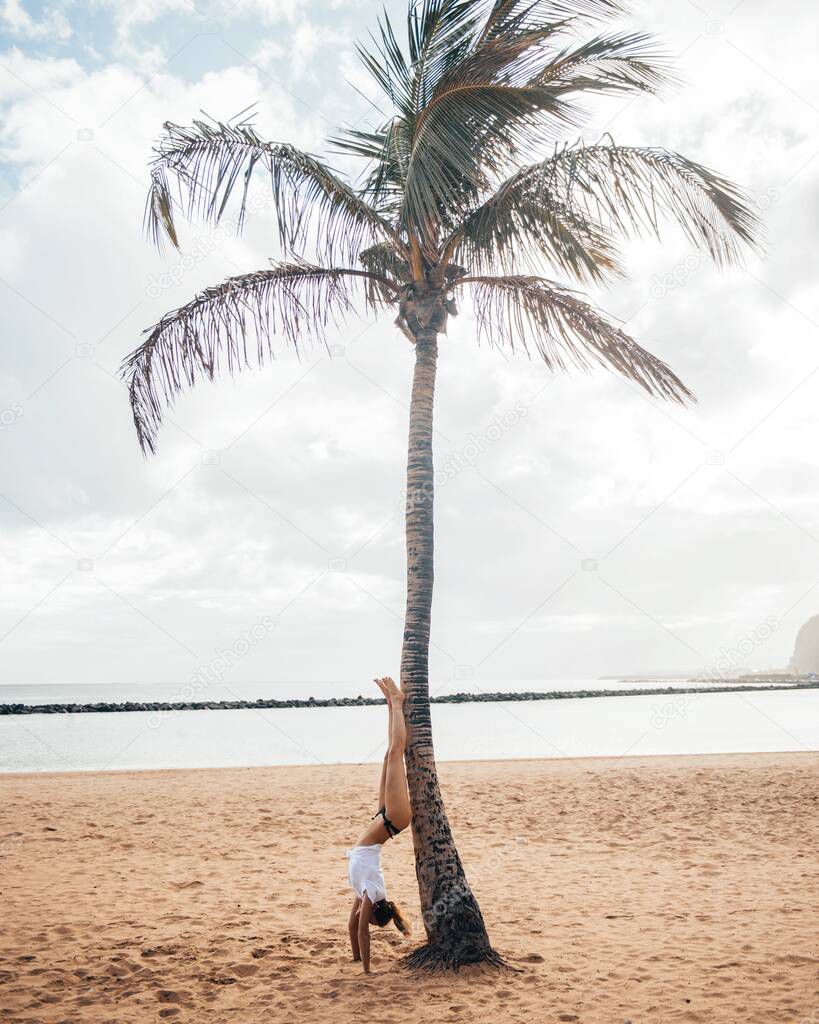 Handstand near palm tree on sandy beach, Tenerife Spain